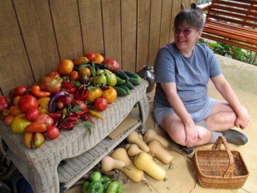 An older woman sitting next to a table piled high with vegetables